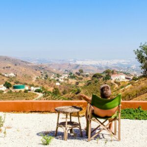 Man Sitting on Green Chair Near Trees and Mountain Under Blue Sky at Daytime